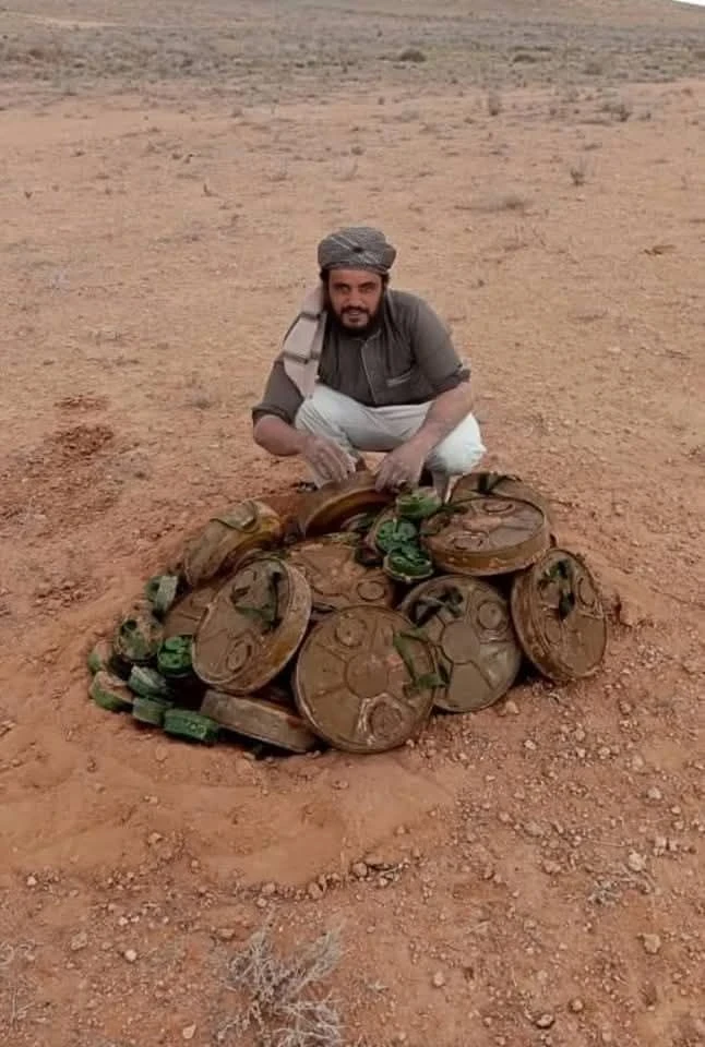 بطل الألغام في صورة تذكارية أمام مجموعة من الألغام التي فككها